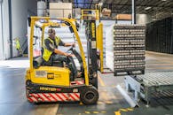A warehouse worker maneuvers a forklift to transport crates for brewing company storage.